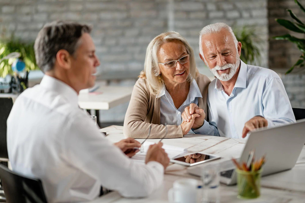 happy-senior-couple-holding-hands-using-laptop-while-having-meeting-with-financial-advisor-office-se